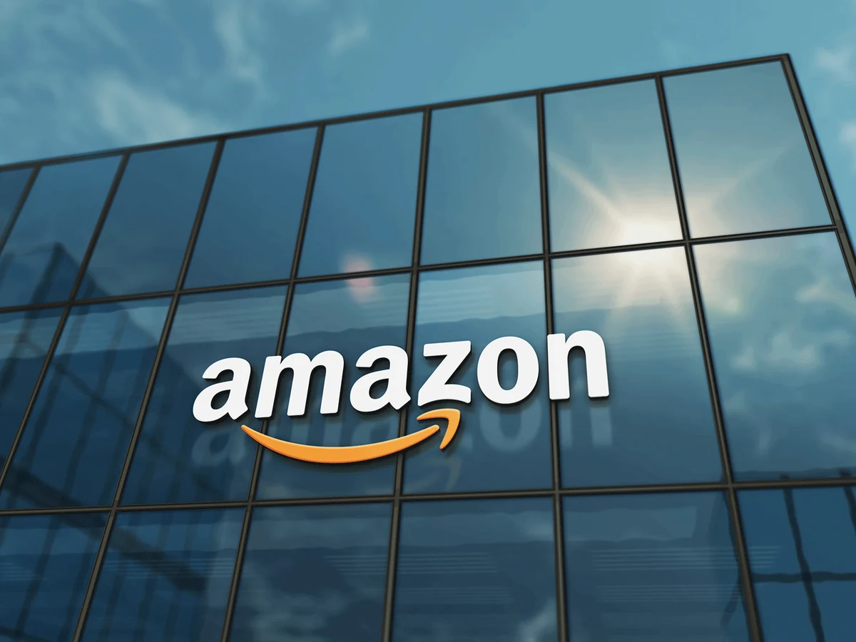 The Amazon logo on the glass facade of an office building, shot from below against a blue sky