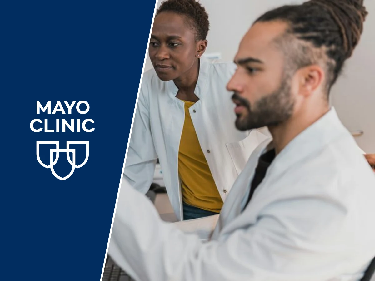 Two clinicians in white coats discussing something on a monitor, beside a navy panel carrying the Mayo Clinic logo